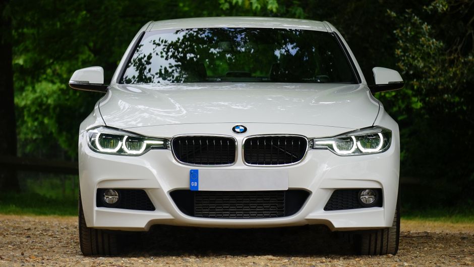 Elegant white luxury car with prominent grille and sleek design, set outdoors, showcasing modern headlights.